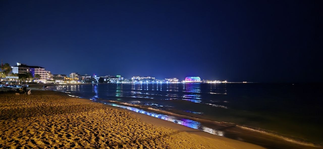 Ruhiger Sandstrand an der türkischen Riviera bei Nacht mit beleuchteten Hotels nahe Alanya